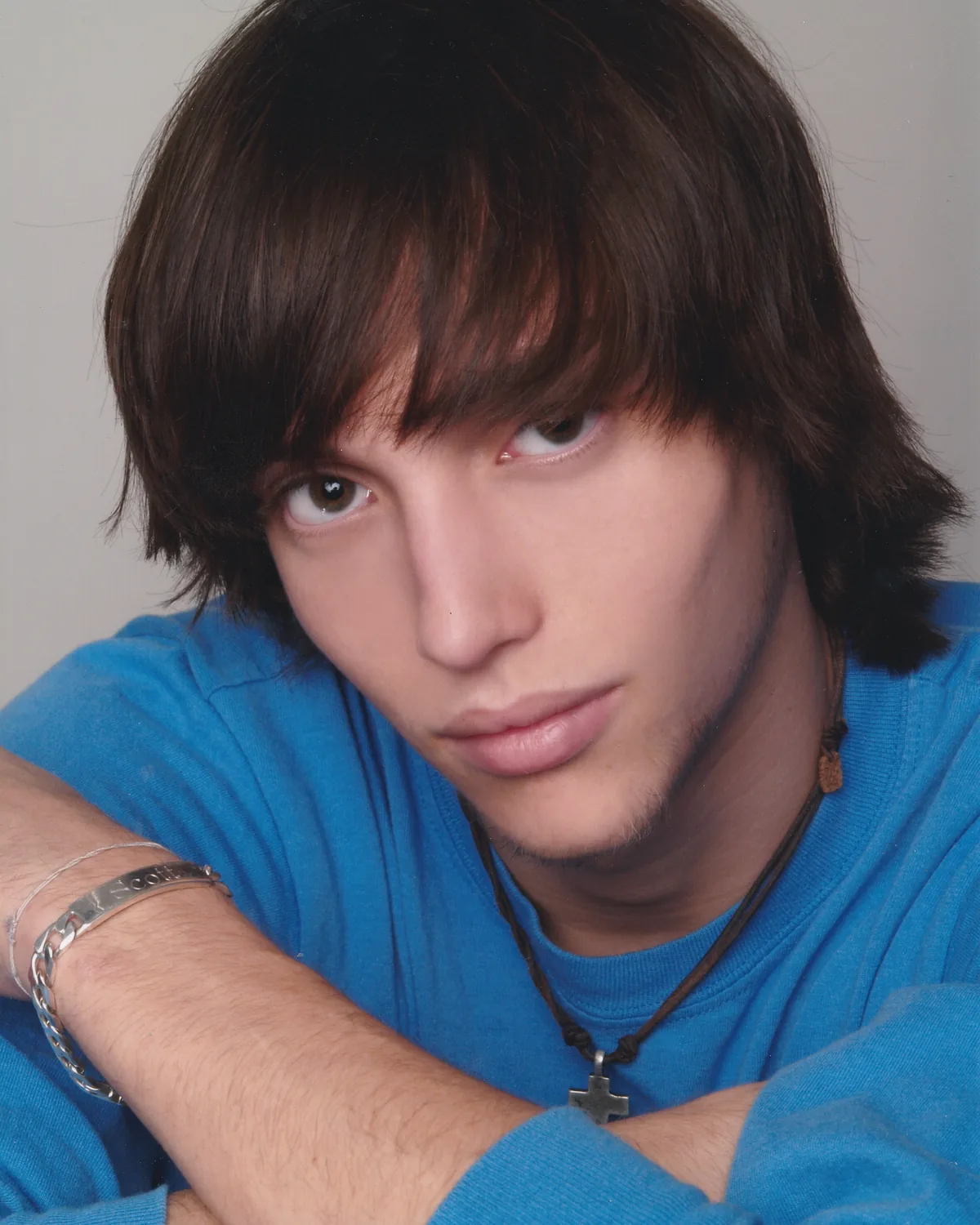A studio portrait of Scott Hancock in a blue shirt, wearing a cross on a chain, his arms folded in front of him.
